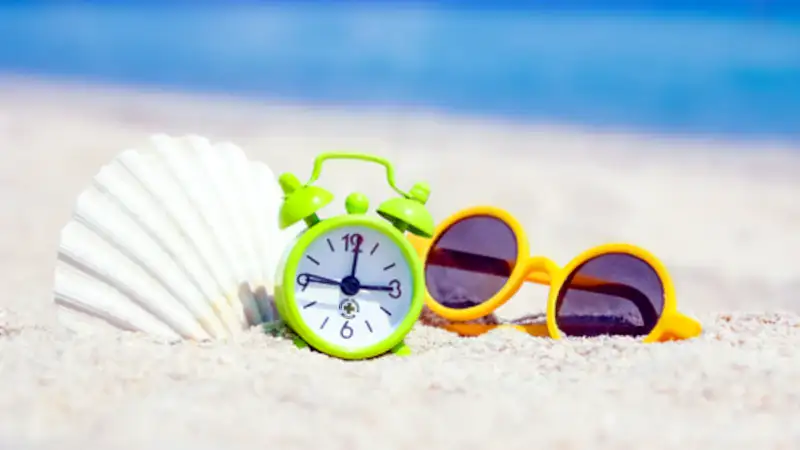 orari mese di agosto, occhiali e orologio su spiaggia